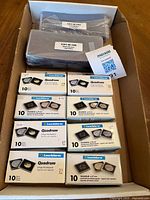 Photo showing multiple packs of Leuchtturm Quadram coin holders in assorted sizes along with three stacks of C01-M-100 banknote holders in plastic packaging.