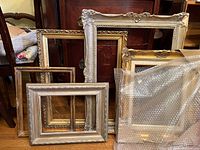 Photo showing 5 decorative picture frames stacked and leaning together, including various gold and silver tones with ornate designs.