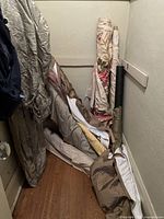 Photo showing multiple bolts of fabric including cream floral, bronze/taupe shiny fabric, light blue with gold pattern, and other textiles leaning against the wall