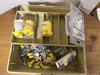 Beige compartmentalized plastic toolbox containing various electrical hardware items including yellow plugs, assorted wire nuts, metal connectors, dimmer switch parts in packaging, and other miscellaneous small electrical components.