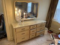 Front view of the dresser with mirror, showing cream color, glass top, decorative carvings, and metal drawer handles.