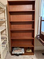 Full view of bookshelf against a wall with some objects placed on bottom shelf and drawer closed.