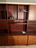 Photo of the middle unit of the three-piece media cabinet with open shelves, some small motorcycle models, lower cabinets, and a removable top shelf piece.