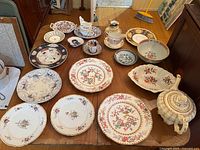 Full view of the antique china lot on wooden table showing variety of plates, bowls, teapot, and teacups