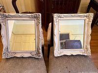 Front view of the two antique-style square mirrors placed side by side on a chair showing ornate floral carved frames in distressed off-white.