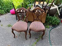 Front view of two antique wooden chairs with carved backs and striped upholstered seats, showing overall condition and design.