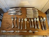 Complete layout of silverware on wooden table showing knives, forks, and spoons in groups by type and size.
