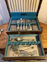 Overall view of the silverware set in its original blue velvet-lined box showing various forks, spoons, butter knives, and serving utensils.
