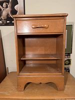 Full front view of the solid wood MCM bedside table showing the drawer, open shelf, wooden handle, and base design.