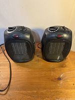 Front view of two black portable space heaters showing control knobs and protective mesh front grille.