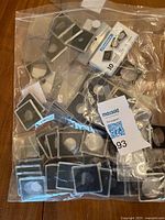 Clear plastic coin holders of multiple sizes, some with black or gray inserts, along with a sealed partially used pack of bill holders for paper currency, shown in a clear plastic bag.