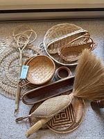 Multiple woven baskets of various shapes and sizes along with a natural fiber broom with a wrapped handle.