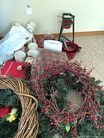 Overview of various Christmas decor items on carpet including wreaths, tree stands, ceramic mugs, glass candle holders, and decorative bowls.
