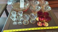 Photo showing all glassware items including large clear bowls, clear parfait bowls, and small clear and ruby red wine glasses arranged on a table with a measuring tape