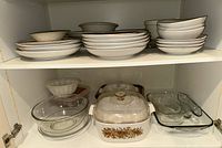 Shelves with stacked ceramic plates and bowls, assorted clear glass casserole and bakeware including a CorningWare casserole dish with floral pattern and glass lid
