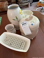 Various ceramic decor items shown on table including floral vase, lidded container, white ribbed bowl, and small rectangular dish with grid