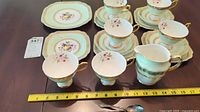 Complete view of china tea set with cups, saucers, small plates, and three teaspoons laid out with ruler for scale.