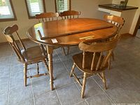 Oval solid maple kitchen table with five matching chairs around it. The table has turned legs and medium wood finish.