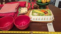 Red mixing bowls, stack of napkins/placemats, rectangular covered ceramic dish with vegetable decoration