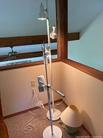 Two white floor lamps side by side, one taller and one shorter, with three adjustable spotlight fixtures each, and a small table lamp with green base and cream shade on the floor nearby.