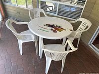 White plastic patio table with four matching white plastic chairs surrounding it on a patio with tile flooring. Table is round with a solid surface.