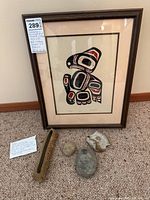 Framed Indigenous serigraph print in traditional style along with three vintage ceramic and fossil items placed on beige carpet.