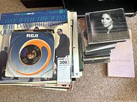 Stack of LP records and pile of CDs with a 45 RPM disc visible