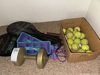 Tennis rackets in covers, ankle weights, dumbbell weight, jump rope, and box of tennis balls on carpet