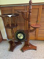 Full view of two wooden plant stands and hanging wall clock with zodiac symbols in front of wooden closet doors.