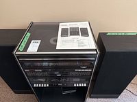 Front view of vintage Sears stereo rack system with turntable covered by glass on top and two speakers alongside. Original manual placed on top of stereo rack.