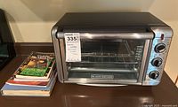 Front and side view of Black+Decker toaster oven with stack of cookbooks beside it on the countertop.