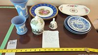 Full view of Wedgwood jasperware vases, assorted plates, covered jar, and decorative bell arranged on table with measuring tape for scale.