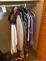 Wide view of women's clothing hanging in closet, showing various coats and a purple blouse, with slippers below