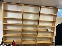 Four tall wooden bookshelves lined up against a wall in a basement, some shelves holding a few items and showing light use wear.