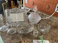 Photo of assorted glassware on countertop showing candlesticks, frame, swan dishes, candy dish, decanter, and small container