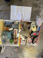 Top view of two plastic bins filled with assorted screws, fasteners, and painting supplies including rollers and a paint mask.