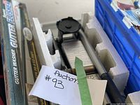Close-up photo showing a hydraulic bottle jack and packaged gutter washer tool along with part of the lot's auction number tag.