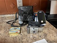 Overview of all items in lot on countertop: Canon camera, Dr Ho blood pressure monitor, Tento binoculars, tin box.