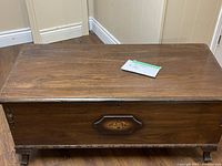 Closed wooden cedar chest with a floral decorative panel on the front.