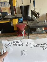 View of Dremel Moto Saw compact scroll saw and red metal vice on a workbench with handwritten label describing items.