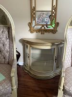 Front view of curved glass buffet cabinet between two chairs, showing glass shelf and door