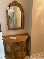 Front view of wooden hallway table placed in corner with ornate carved detail and matching mirror above.