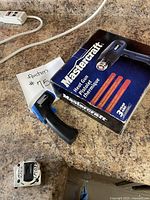 Photo showing a black Mastercraft heat tool in its original box and a black infrared thermometer placed on a kitchen counter.