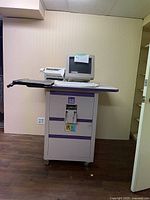 ISP 950 Instant Publisher machine with CRT monitor, fax machine on the right, and cabinet with ISP 950 branding, shown in a room against a wall.