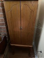 Full front view of the standing wood jewellery cabinet showing two decorative front doors with metal handles and curved legs on the bottom.