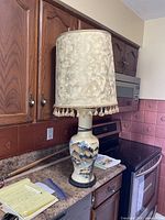 Full view of the ceramic table lamp with fabric tassel lampshade placed on countertop near stove and cabinets.