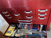 Front view of red metal tool box with multiple drawers, showing tools inside some drawers including packaged screwdrivers and socket sets.