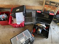 Photo of assorted tool cases including three metal red toolboxes, three black/gray plastic toolboxes, two nut and bolt organizers, staple tool, Xmas lights, and a Black & Decker power tool case.
