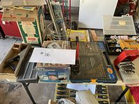 Photo showing table with wet sharpener box, toolbox with drill bits, hand planer, and other tools.