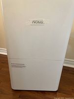 Front view of the NOMA dehumidifier showing plain white exterior and brand name taped on the front.